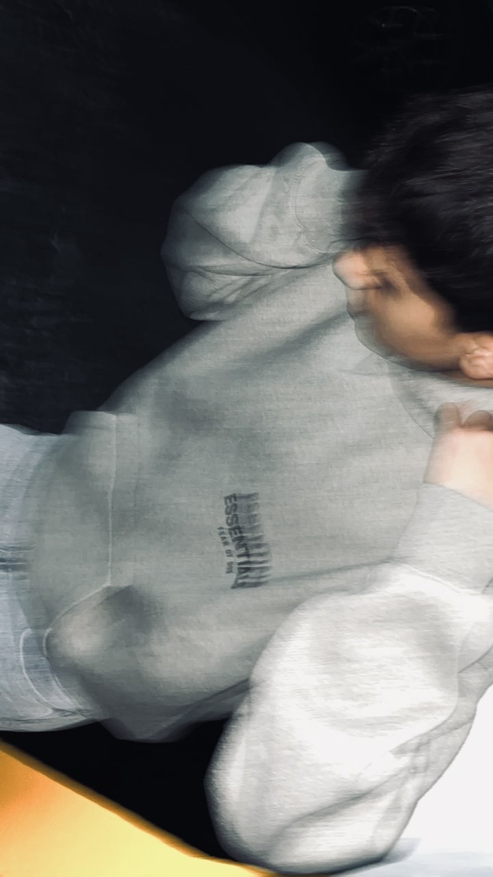 Detalle en movimiento del hoodie Essentials gris con logo al centro de la espalda.