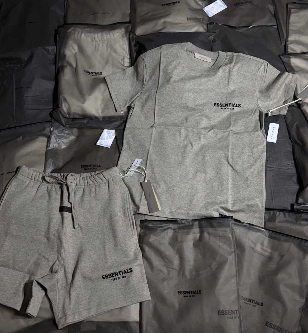 Conjunto Essentials de playera y short en gris medio con etiquetas originales.