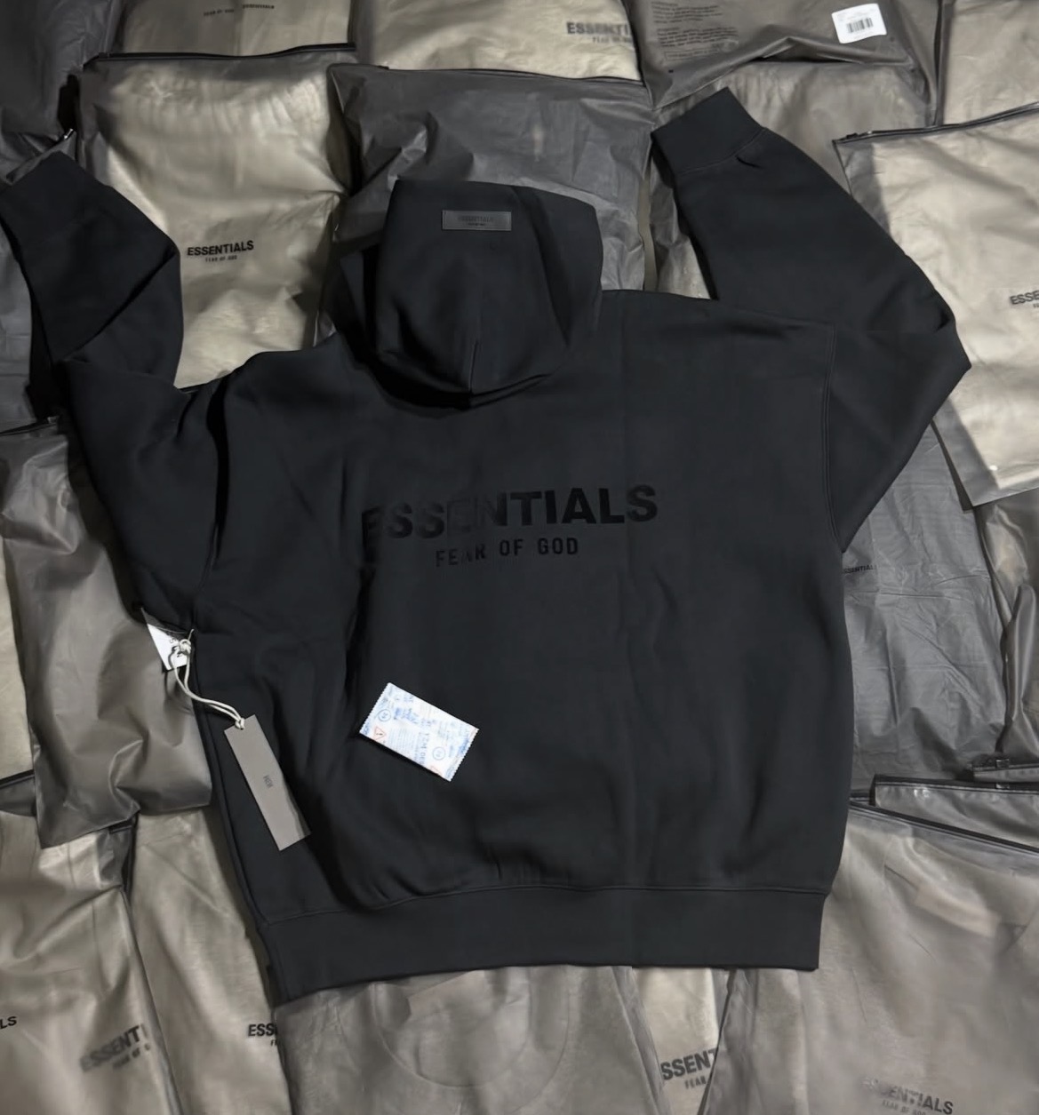 Hoodie Fear of God Essentials en negro con logo tono sobre tono y etiquetas.
