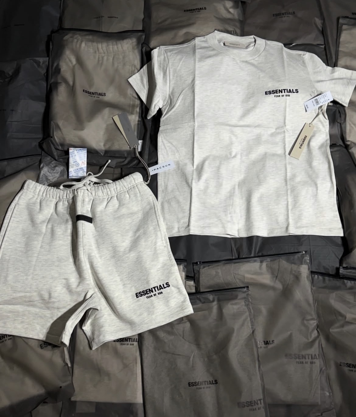 Conjunto Essentials de playera y short en gris claro jaspeado con etiquetas.