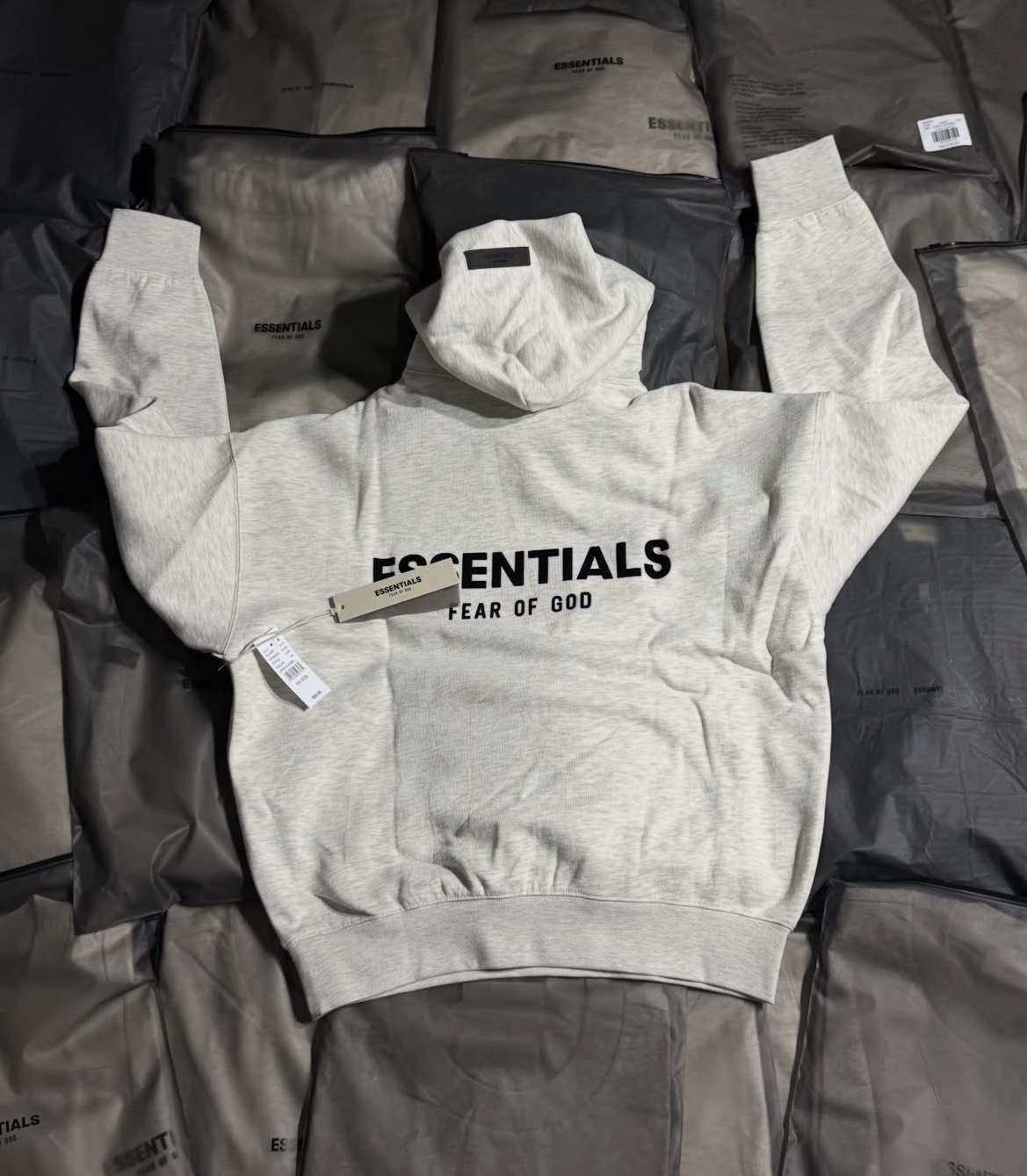 Hoodie Essentials gris claro sobre empaques originales.